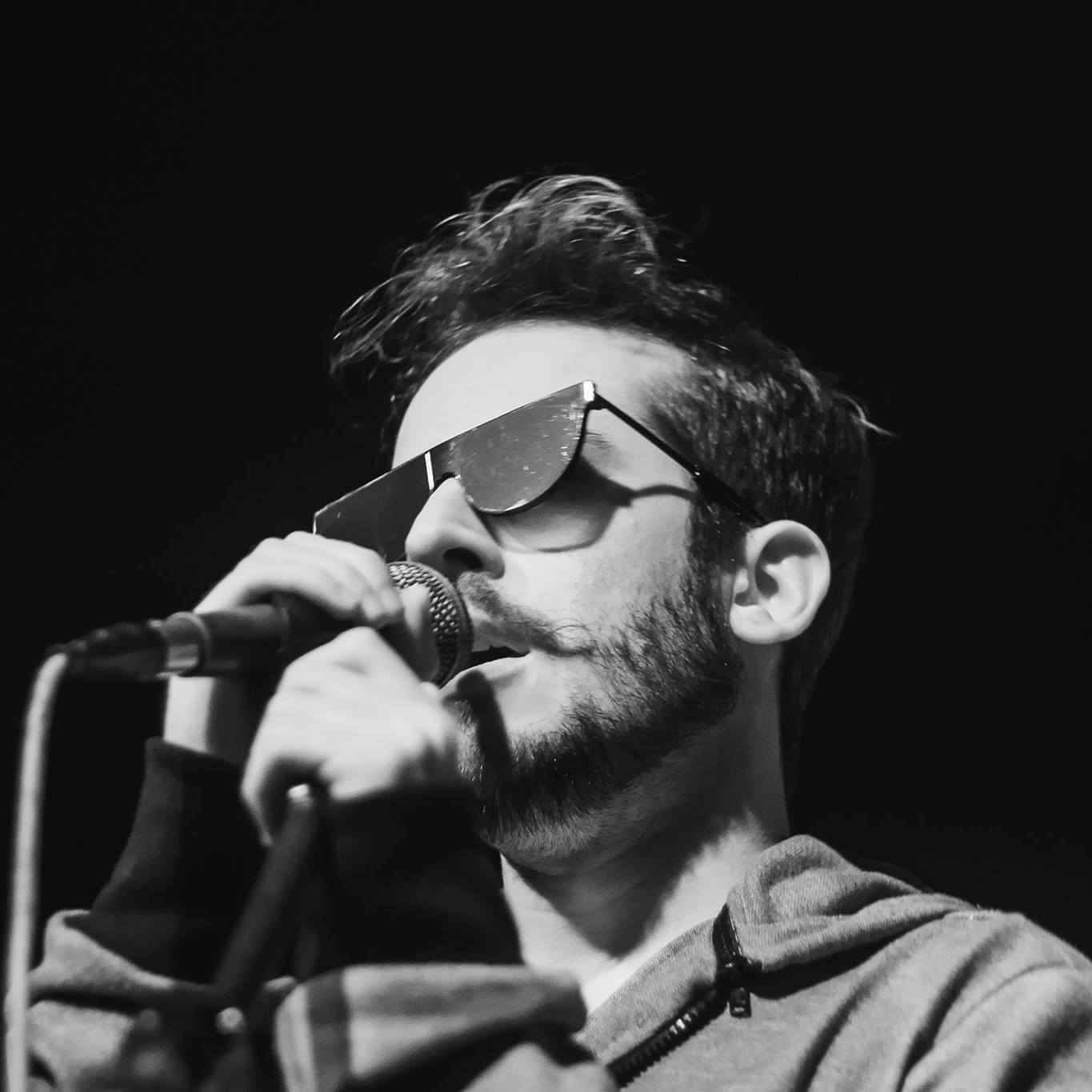 Imagem de divulgação oficial de Jimmy Andrade em preto e branco, de óculos, cantando.